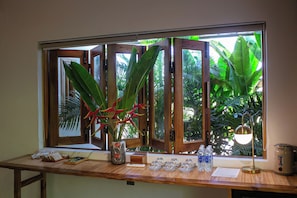 Uma mesa de madeira com uma janela, um vaso com flores vermelhas e um bebedouro.