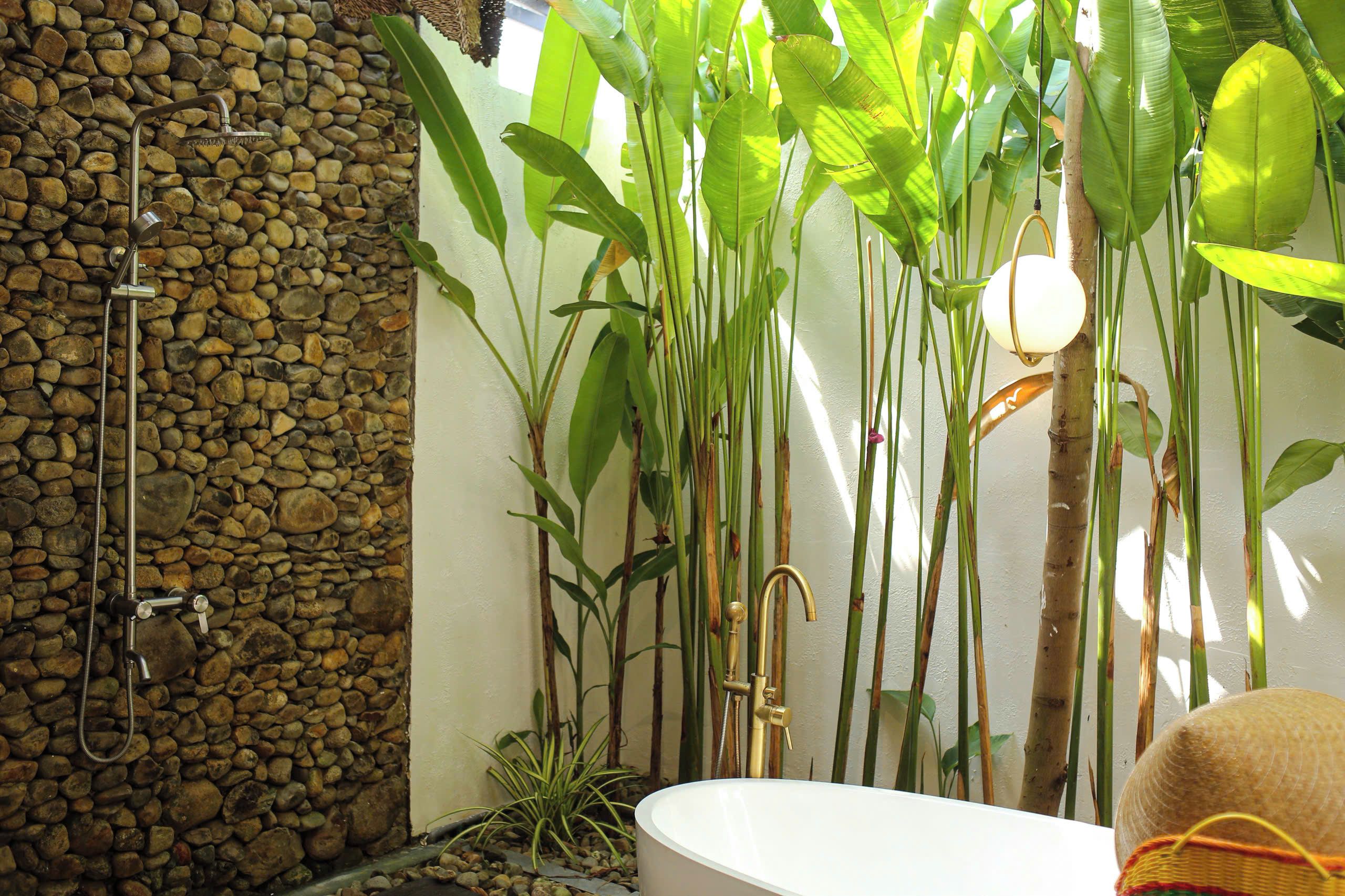 Une salle de bain avec un mur en pierre, une douche, une baignoire et diverses plantes.