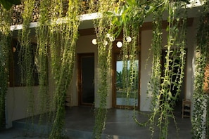 Un espacio exterior techado con plantas colgantes y una puerta que da a un área interior.