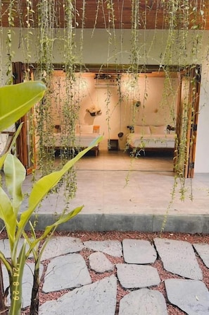 Quarto com cama, uma mesinha e plantas penduradas.