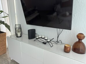 A white entertainment unit with a flat-screen TV, a black speaker, and decorative items including candles and a glass candle holder. - Luxury beachfront apartment (Luquillo)