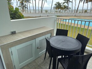 A balcony with a pool view, outdoor seating, and a white railing. - Luxury beachfront apartment (Luquillo)