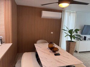 A room with a wooden slat wall, a ceiling fan, an air conditioning unit, a table with a vase and remote control, a plant, and a TV on a cabinet. - Luxury beachfront apartment (Luquillo)