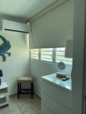A small bathroom with a vanity, a stool, a mirror, and an air conditioning unit. - Luxury beachfront apartment (Luquillo)
