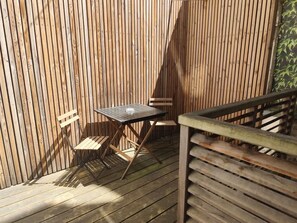 Une terrasse en bois avec une table et des chaises, une rambarde en bois et un mur composé de panneaux de bois verticaux.