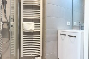 Une salle de bain avec une douche à parois de verre, un porte-serviettes et un meuble blanc doté d’une poignée.