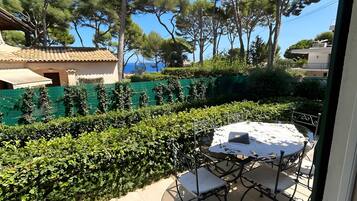 A patio with a table and chairs, surrounded by greenery and trees.