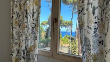 A window with floral curtains, a view of trees and a clear sky.