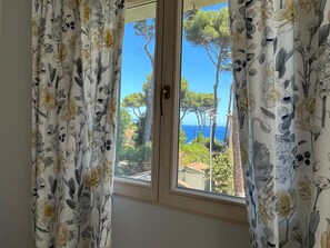 A window with floral curtains, a view of trees and a clear sky. - Villa 'Sea View Cap D’Antibes' with Sea View, Wi-Fi and Air Conditioning (Antibes)