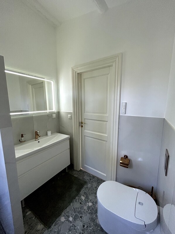 A bathroom with a white sink, a mirror with lights, a toilet, and a door.