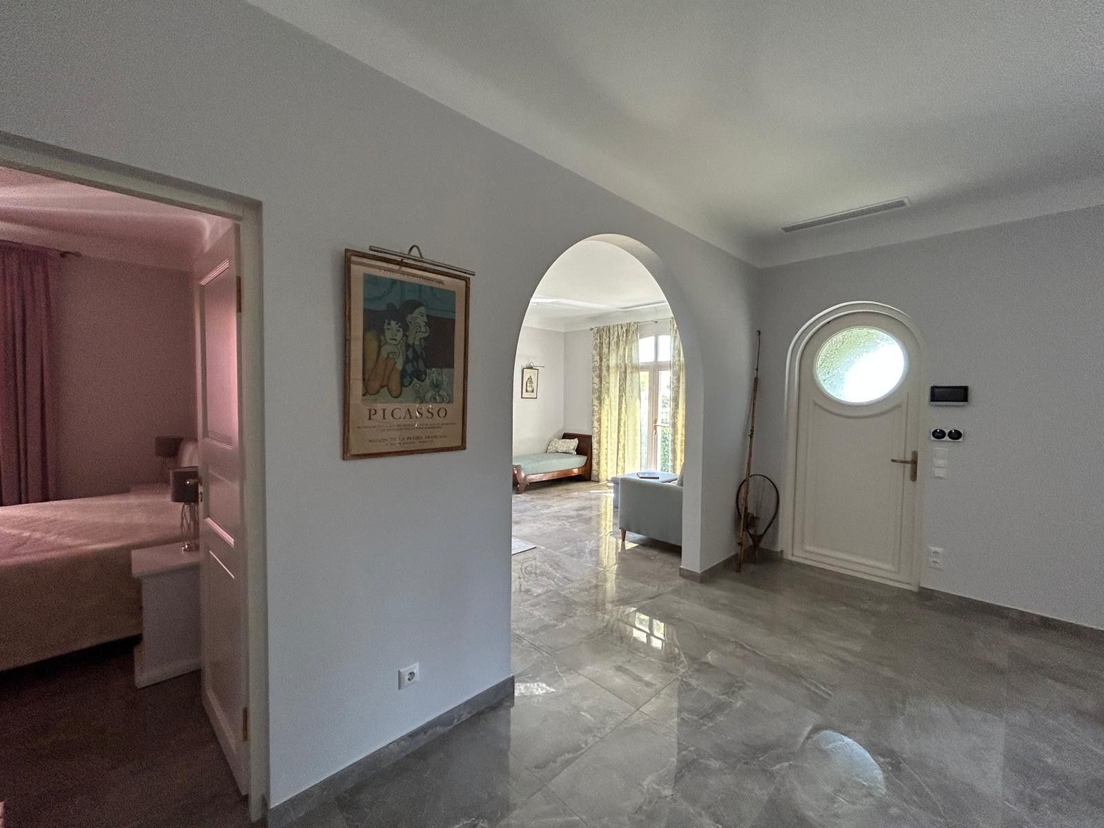 A hotel room with a bed, a door with a circular window, and a framed artwork on the wall.