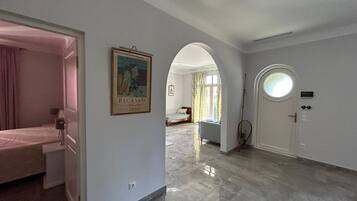 A hotel room with a bed, a door with a circular window, and a framed artwork on the wall.