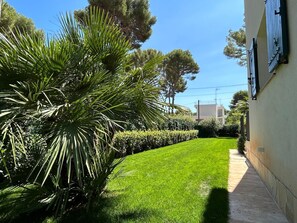 Une pelouse bien entretenue, avec un chemin qui mène à un bâtiment à la façade blanche et aux volets fermés.