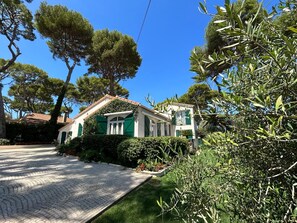 A two-story house with a tiled roof, green shutters, and a paved driveway.