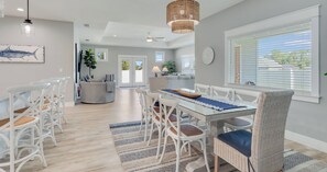 A modern dining area with a glass table, white wicker chairs, and a woven pendant light. - 4BR Home With Fenced Yard & Grill (Panama City Beach)