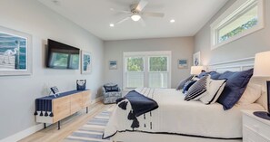 A bedroom with a bed, bedside tables, a chair, a TV, and artwork on the walls. - 4BR Home With Fenced Yard & Grill (Panama City Beach)