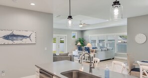 A modern kitchen with a central island, a dining area with a white table and chairs, and a living room with a sofa and a coffee table. - 4BR Home With Fenced Yard & Grill (Panama City Beach)