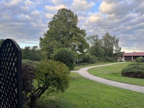 Ein gepflasterter Weg schlängelt sich durch einen gepflegten Garten mit verschiedenen Bäumen und Sträuchern.