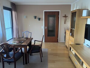 Ein Essbereich mit einem Holztisch und -stühlen, einer Tür mit rauer Glasscheibe und einer Holzvitrine mit Fernseher.