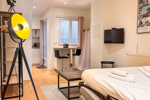 Quarto de hotel com uma cama, uma mesa com duas cadeiras, uma televisão e um tripé com luz.