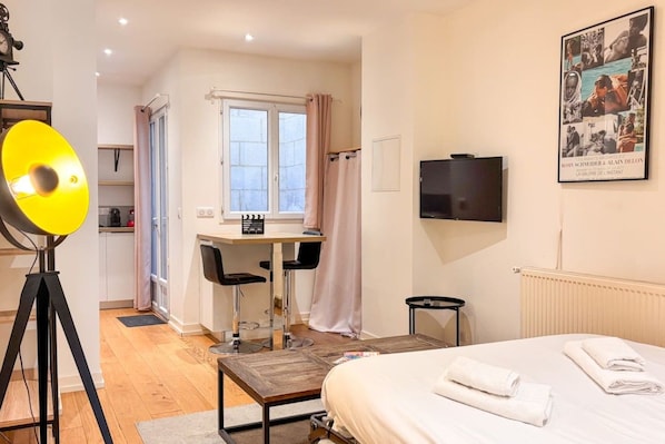 Quarto de hotel com cama, escrivaninha, cadeira, televisão e um pôster na parede.