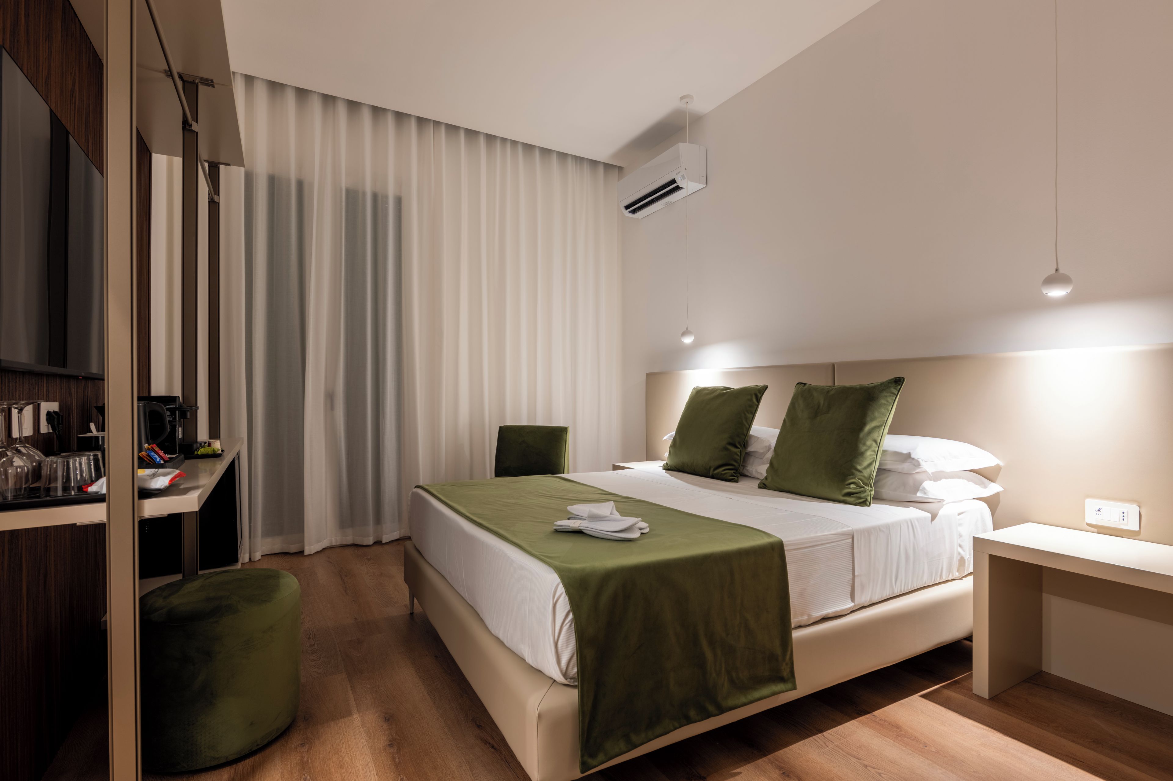 Moderni hotellihuone, jossa on sänky, yöpöytä ja työpöytä tuolilla.