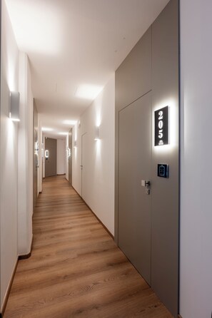 A hotel corridor with a wooden floor, white walls, and doors with illuminated numbers. - Gallery Luxury (Palermo)