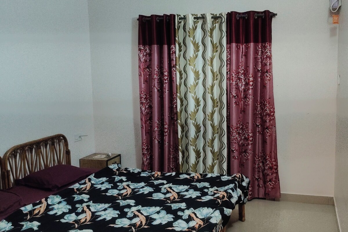 A small bedroom with a bed, a chair, and a nightstand. There are curtains on the window.