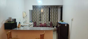 A kitchen with a counter, chairs, a refrigerator, and a window with curtains. - Reliance sea mist (Morgoa)