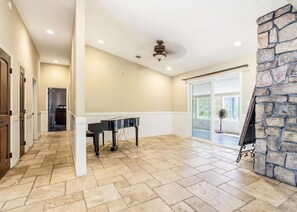 A spacious room with a piano, a stone fireplace, and a view through a glass door.