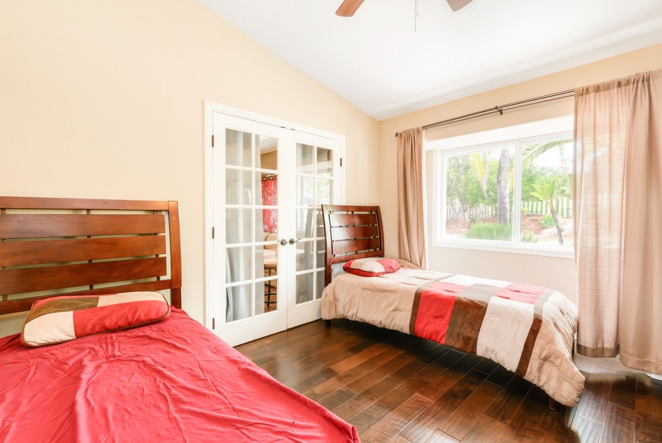 A bedroom with two beds, a sliding glass door, a window with curtains, and a ceiling fan.