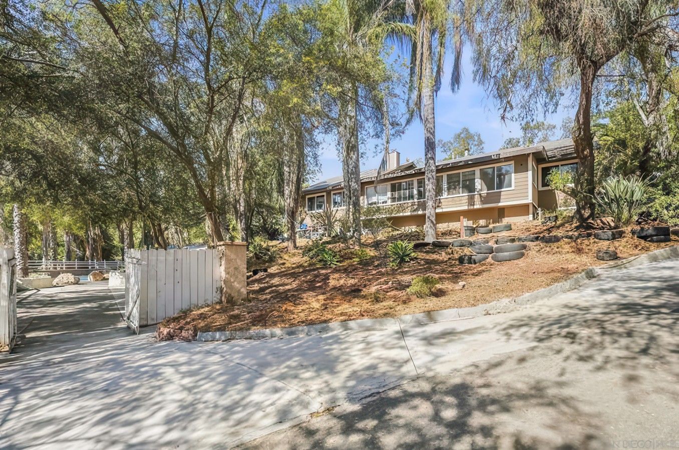 Une maison moderne à deux étages, dotée d’une allée pavée et entourée d’arbres, avec une zone délimitée par une clôture.