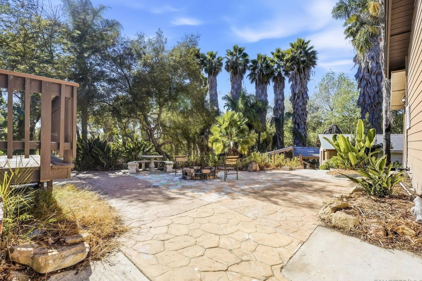 Un patio con suelo de piedra, una pérgola de madera y un conjunto de asientos.
