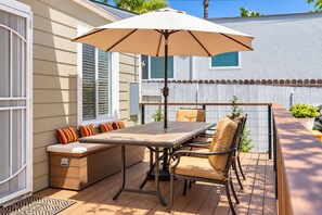 Eine Terrasse im Freien mit Tisch, Stühlen, einer Bank und einem großen Sonnenschirm.