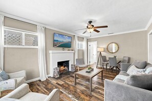 Ein Wohnzimmer mit Kamin, Deckenventilator und Fernseher, der eine Strandansicht zeigt.