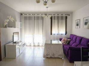 Ein modernes Wohnzimmer mit einem violetten Sofa, einem Flachbildfernseher, einem Glastisch und einem Esstisch.