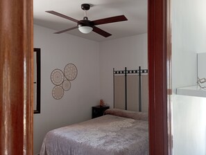 Ein Schlafzimmer mit Bett, Deckenventilator, Wandspiegel und dekorativen Wandbildern.