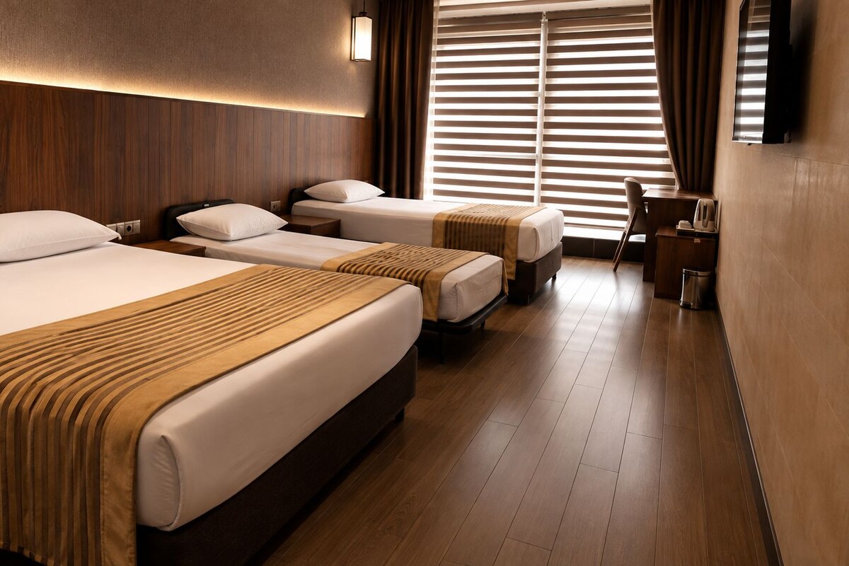 A hotel room with three beds, a desk, and a TV.