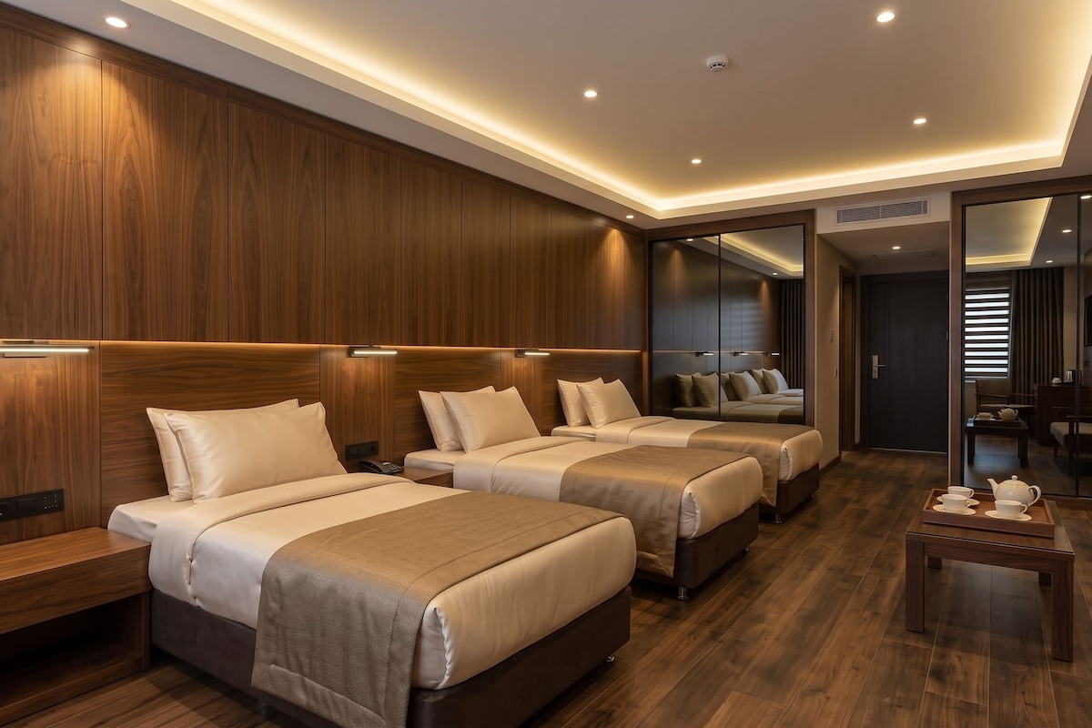 Habitación de hotel con dos camas, paneles de madera, una mesita con juego de té y una puerta corredera que da a un baño.