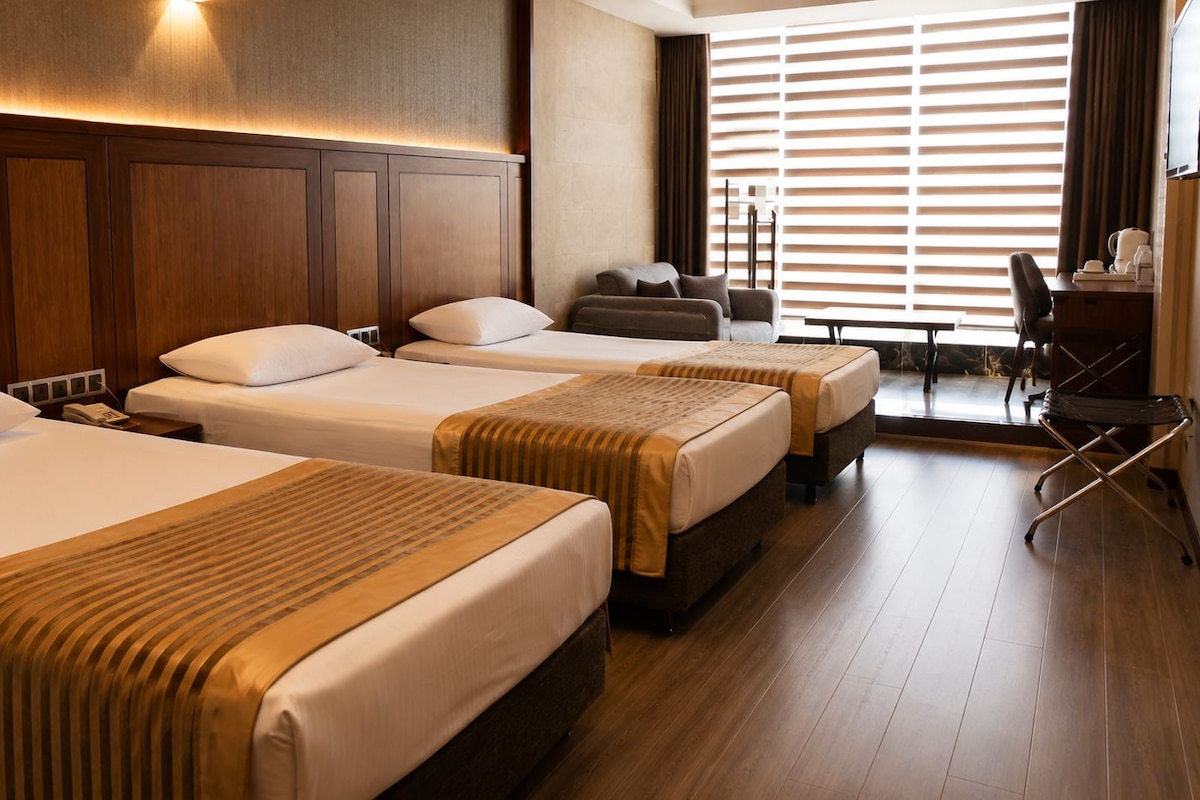 A hotel room with three beds, a desk, and a chair.