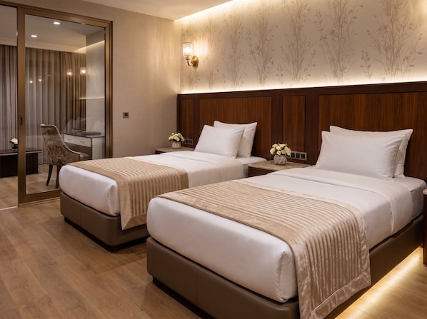 Habitación de hotel con dos camas, un espejo, una mesita de noche con lámpara y cabecera de madera.