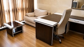 Un espacio de oficina moderno con un escritorio de madera, una silla de oficina blanca, una mesita auxiliar pequeña y un sofá color beige.