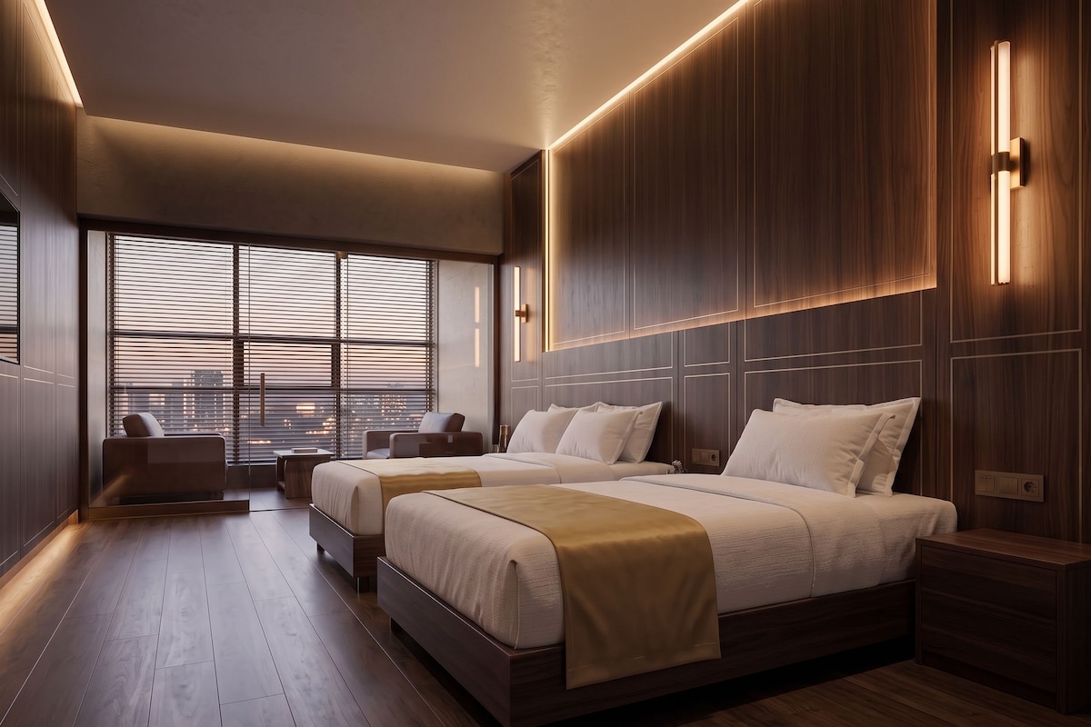 A modern hotel room with two beds, a seating area, and large windows.