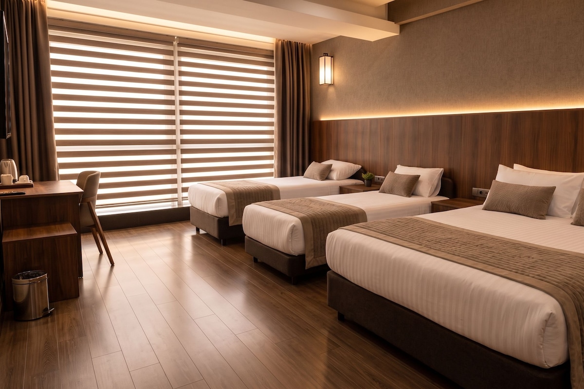 Una habitación de hotel con dos camas, un escritorio y un ventanal grande con persianas.