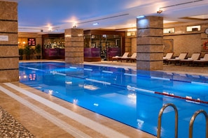 Una piscina interior con divisiones de carril bien definidas, una zona de descanso con sillas y un indicador de temperatura visible.