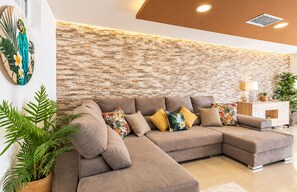 A modern living room with a sectional sofa, decorative pillows, a wall-mounted artwork, and a plant. - Stunning Costa Adeje Villa: 3BD, Private Pool, Terrace & AC (Costa Adeje)