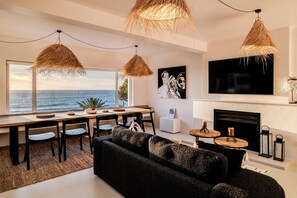 A modern living room with a large window overlooking the sea, a fireplace, and a dining area with a view. - Camps Bay 6 Bed Ocean Views and Pool Villa Kai (Cape Town)