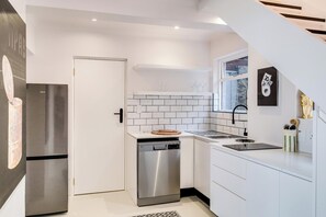 A compact kitchen with white cabinetry, a stainless steel refrigerator, a dishwasher, and a window with a view. - Camps Bay 6 Bed Ocean Views and Pool Villa Kai (Cape Town)