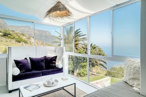 A modern living room with a sofa, coffee table, and large windows offering a view of the sea and mountains. - Camps Bay 6 Bed Ocean Views and Pool Villa Kai (Cape Town)