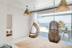 A modern interior with a hanging chair and a woven floor lamp, a view of the ocean, and a balcony with outdoor seating. - Camps Bay 6 Bed Ocean Views and Pool Villa Kai (Cape Town)